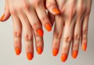 Dłonie z pomarańczowymi paznokciami w różnych odcieniach, od neonowych po pastelowe
